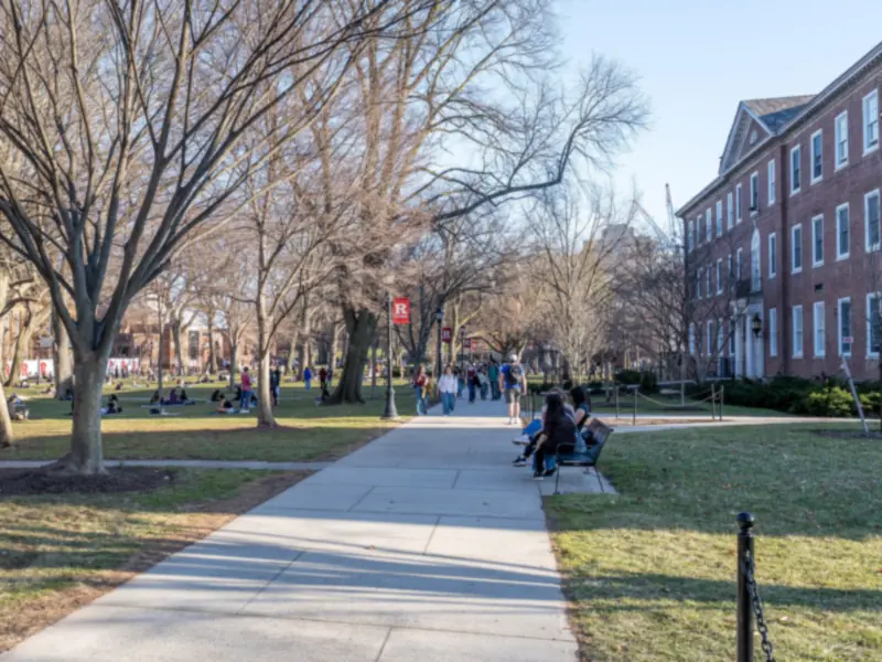 Students walking along a tree-lined path on the Rutgers–New Brunswick campus on a sunny late-winter day
