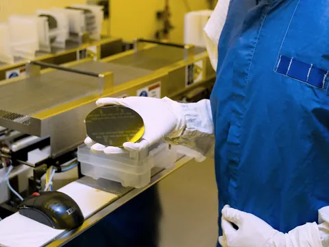 Gloved hands holding a finished silicon wafer in a cleanroom